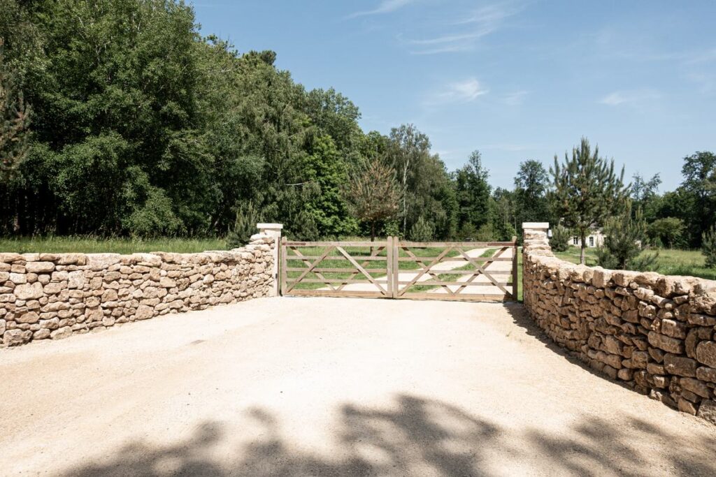 Muret en pierre sèche et portail agricole en bois à cinq barreaux, entrée de propriété à Bourgueil